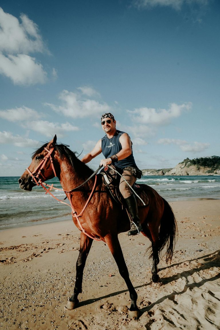 A man leisurely rides a horse along a sunny beach, capturing a serene coastal moment.