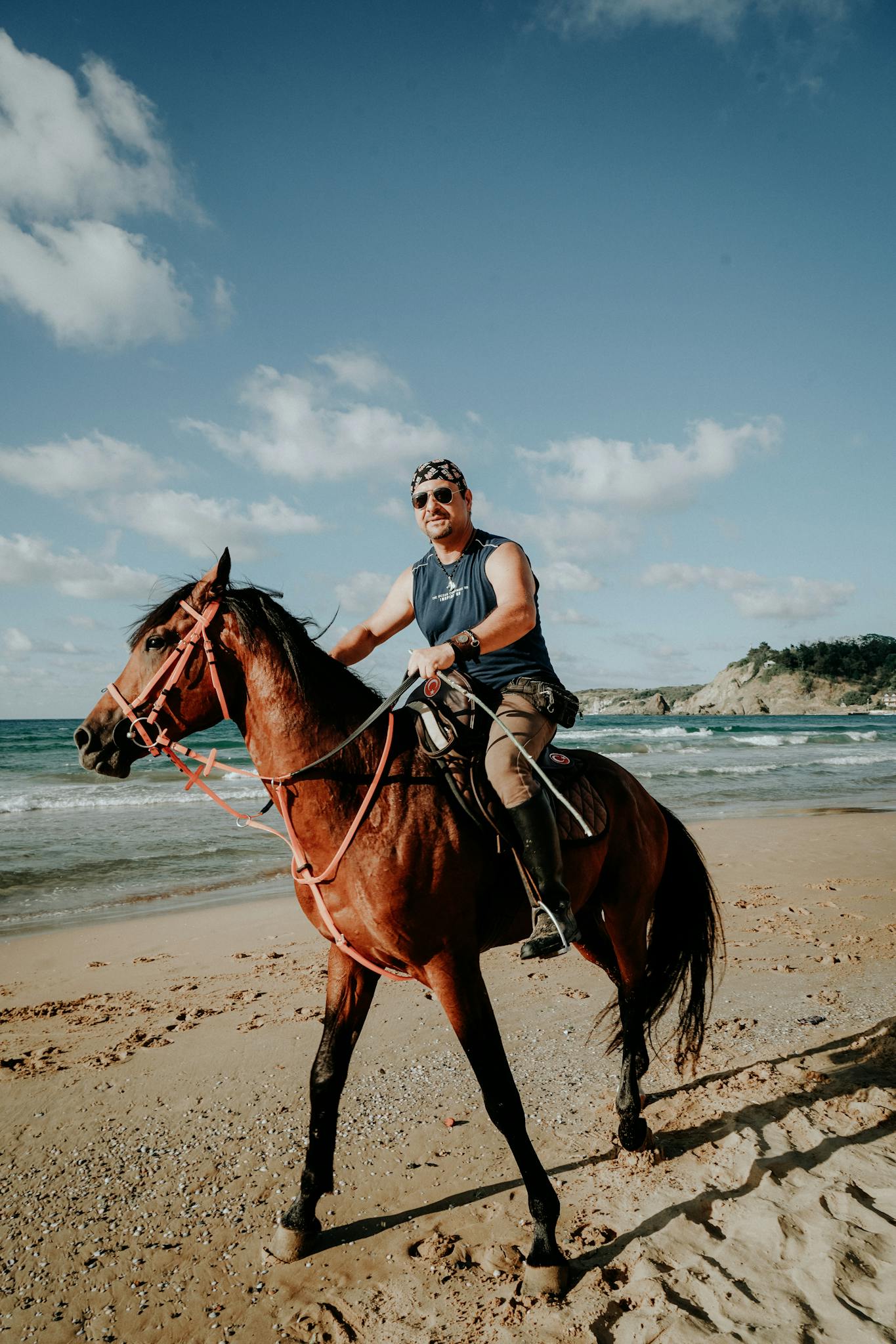 A man leisurely rides a horse along a sunny beach, capturing a serene coastal moment.