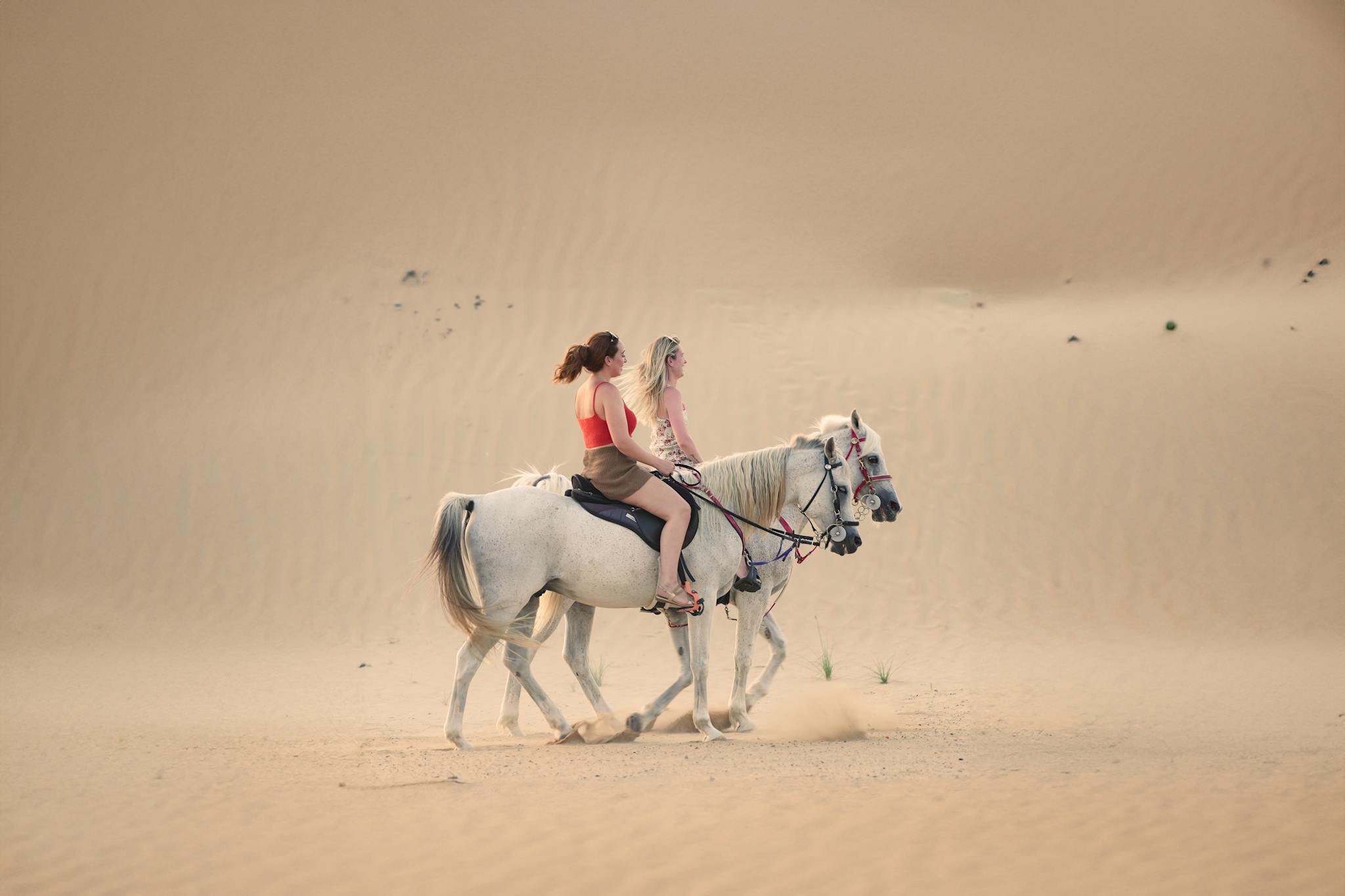 Two women riding horses through the dunes of Dubai's desert, capturing serene beauty and adventure.